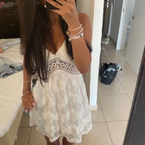 Vit spetsklänning med v-ringning - Söt vit kortklänning med v-ringning och spetsdetaljer. Klänningen är ärmlös och har ett romantiskt mönster med broderade partier. Perfekt för sommarens varma dagar. Köpt utomlands!!