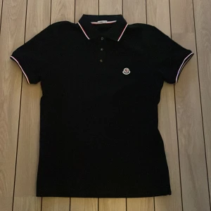 Svart pikétröja från Moncler - Säljer en svart pikétröja från Moncler med klassisk krage och knappar framtill. Skick 10/10 använd typ 2 gånger, säljer då den är för stor på mig