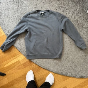 Grå/turkos sweatshirt från H&M Essentials - Enkel och stilren grå sweatshirt från H&M Essentials, modell No 5. Tröjan har relaxed fit, rund halsringning och ribbade muddar vid ärmslut och nederkant. Perfekt för en chill och avslappnad look.