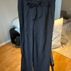 Svarta byxor med knyt från Amisu - Svarta byxor från Amisu med hög midja och knytband i midjan. Byxorna har raka ben och är tillverkade i ett mjukt tyg som känns bekvämt. Perfekta för en stilren och enkel look. 🩷 Storlek 34 🌸