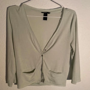 Ljusgrön kofta - Säljer en tunn ljusgrön kofta från H&M med v-ringning och två små fickor framtill. Koftan har lång ärm och knäpps med knappar. Perfekt att slänga över en topp eller linne.