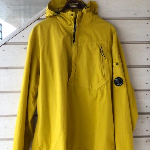 C.P. Company gul jacka, storlek XL - Gul C.P. Company jacka med huva, halvlång dragkedja fram och en ficka på bröstet. Jackan har även C.P. Company-linsen med plastfilmen kvar på vänster arm. Använd vid ett fåtal tillfällen, köpt på NK Göteborg, nyskick.