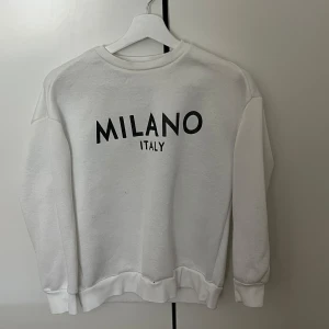 Vit sweatshirt Milano Italy Shein - Vit sweatshirt från Shein med svart text 'MILANO ITALY' på bröstet. Klassisk rund halsringning och långa ärmar med ribbade muddar. Perfekt för en chill och stilren look. Mjuk och skön, passar till jeans eller leggings.