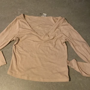 Beige v-ringad topp från H&M Divided - En stilren beige långärmad topp från H&M Divided. Toppen har en djup v-ringning och är tillverkad i mjuk bomull, perfekt för en enkel och clean look. Passformen är normal och den neutrala färgen gör den lätt att matcha med olika outfits.