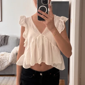 Vit volangtopp med v-ringning och öppen rygg - Säljer en söt vit topp med volangärmar och v-ringning fram. Toppen är croppad och har en öppen rygg med knytband. Perfekt för en snygg vardags outfit.☀️