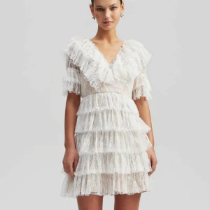 Vit volangklänning i spets - Superfin vit kortklänning med flera lager volanger och v-ringning. Klänningen är ärmlös och har spetsdetaljer över hela. Nypris 2800 kr, helt ny med prislapp kvar💕