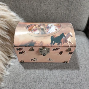 Rosa smyckeskrin med hästmotiv - Superfint rosa smyckeskrin med hästar på locket och sidorna. Insidan är klädd i mjuk rosa textil och har en spegel samt en snurrande hästfigur. Perfekt för att förvara smycken eller småsaker.