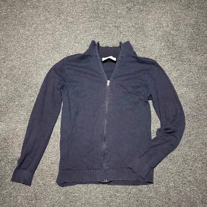 Mörkblå ziptröja från Selected Homme - Mörkblå tröja med dragkedja från Selected Homme. Tröjan har hög krage och långa ärmar. Perfekt för lager-på-lager och enkel att matcha med olika outfits.