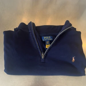  långärmad tröja från Polo Ralph Lauren - Säljer en klassisk mörkblå halvzip tröja från Polo Ralph Lauren med broderad logga på bröstet. Tröjan har hög krage och dragkedja framtill. Perfekt för en stilren och avslappnad look. En tunn tröja med långa armar parfekt för en sval sommarkväll