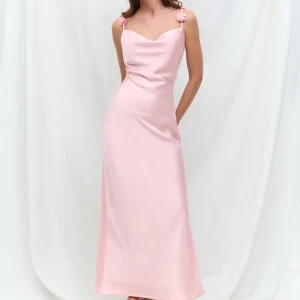 Ljusrosa långklänning med axelband - Säljer en elegant ljusrosa långklänning med smala axelband och söt detalj vid axlarna. Klänningen har en figurnära passform och är tillverkad i ett slätt, glansigt material som ger en lyxig känsla. SLUTSÅLD 