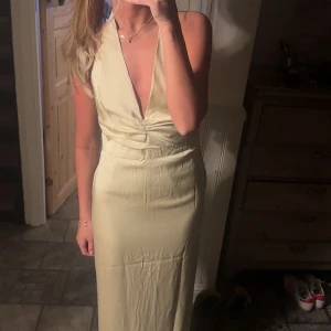 Champange färgad långklänning i satin - Säljer denna champagne färgade långklänning med  v-ringning och halterneck. Klänningen har en figurnära passform och är perfekt för sommarens tillfällen. Materialet är i satin. Den passar mig bra i längden som är ca 170 cm.