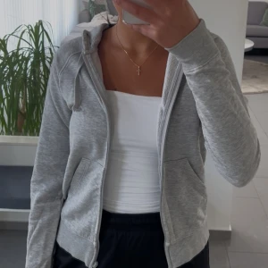 Grå kofta - Säljer en ljusgrå hoodie med dragkedja och huva. 