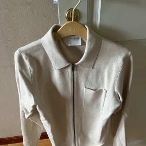 Beige kofta med dragkedja Selected Homme - Stilren beige kofta från Selected Homme med klassisk krage, bröstficka och hel dragkedja framtill. Långärmad och i mjukt bomullsmaterial, perfekt för lager-på-lager och en clean look.