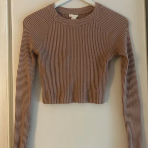 Ribbad croppad tröja från H&M - Säljer en ribbad, croppad tröja från H&M i en snygg beige nyans. Tröjan har lång ärm och rund halsringning, perfekt för dig som gillar en enkel men trendig stil. Passformen är normal och materialet känns mjukt och skönt mot huden.