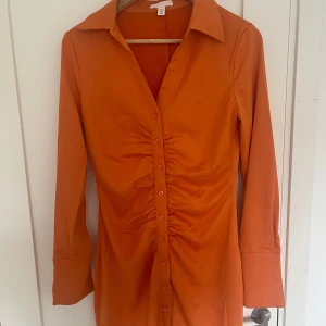 Orange skjortklänning från H&M - Orange skjortklänning från H&M med lång ärm, krage och knappar hela vägen framtill. 
