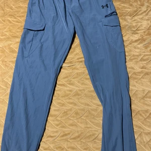 Grå, grön cargobyxor från Under Armour - Ett par stilrena Under Armour-träningsbyxor i silver och grönt, perfekta för gym eller vardag. Bekväm passform, praktiska fickor, och slitstarkt material. Använda en gång, i utmärkt skick.