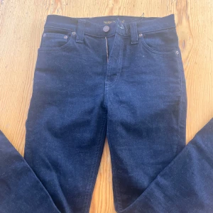 Mörkblå jeans från Nudie Jeans - Säljer ett par mörkblå jeans från Nudie Jeans med klassisk femficksdesign och orangea detaljer. Jeansen har rak passform och är tillverkade i kraftigt denimtyg. Perfekta för dig som gillar stilrena och tidlösa jeans.