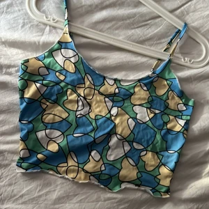 Färgglad mönstrad linnetopp - Säljer en färgglad linnetopp med abstrakt blommigt mönster i blått, grönt, beige och vitt. Toppen har tunna axelband och ärmlös design, perfekt för varma dagar. Storlek S