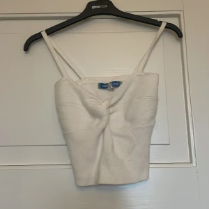 Vit croppad linnetopp från Urban Outfitters - Säljer en vit croppad linnetopp från Urban Outfitters med smala axelband och twistad detalj framtill. Toppen är ribbad och har en tight passform, perfekt för sommaren. Super trendig och perfekt Stockholmstyle top❤️