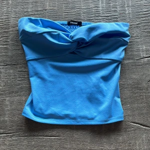 Blå tubtopp med twist från BikBok - Säljer en blå tubtopp från BikBok i storlek XS. Toppen har en snygg twistdetalj framtill och är axelbandslös. Perfekt för sommaren, säljer då jag inte använder den🩵