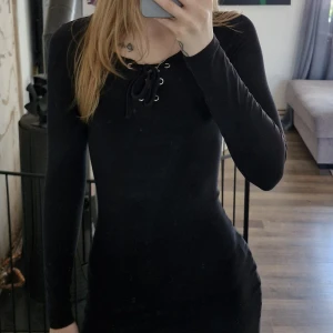 Svart långärmad klänning med snörning från FB Sister - Säljer en svart långärmad klänning från FB Sister. Klänningen har en snygg v-ringning med snörningsdetalj framtill och är figurnära i modellen. Perfekt för dig som gillar enkel men stilren design. Lite blekare än ny.