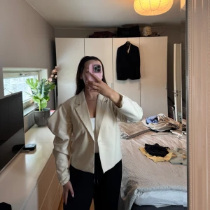 Beige kavaj med puffaxlar  - Säljer en beige kavaj med puffaxlar och oversized passform. Jackan har lång ärm och är tillverkad i ett slätt material. Klassisk krage och enkel design. Knappen på ena sidan har lossnat men går enkelt att sy dit en ny om man vill kunna stänga den. Använd vid 2 tillfällen. 