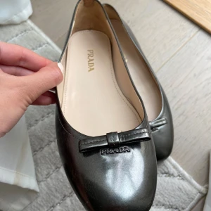 Prada ballerina  - Otroligt fina  ballerinaskor från Prada i glansigt skinn. Färgen är svart/grå/mörkgrön beroende på ljus. Tyvärr för små för mig hade gärna behållt annars. Se defekt på sista bilden, syns knappt irl.  Nypris på ballerinas från Prada idag är runt 10.000kr. Dessa är köpta i Paris för längesen så har inte kvar kvitto. Men garanterar äkthet. Finns att hämta i Vasastan eller frakt mot betalning 🥰. Storlek 37,5 men skulle säga 37