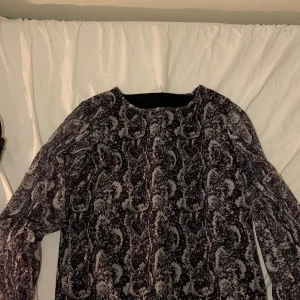 Mönstrad långärmad topp från Lindex - Säljer en cool långärmad topp från Lindex med ett ormskinnsmönster i svart och beige. Perfekt för att ge din outfit en edgy touch. Toppen är gjord i ett lätt och luftigt material.