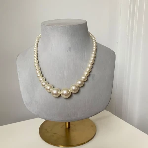 Klassiskt pärlhalsband med dekorativt lås - Elegant pärlhalsband med vita syntetiska pärlor i olika storlekar och ett dekorativt lås med en glittrande sten. Perfekt för att ge en tidlös touch till din stil.
