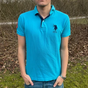 Turkos pikétröja från U.S. Polo Assn. - Säljer en snygg turkos pikétröja från U.S. Polo Assn. med klassisk krage och korta ärmar. Tröjan har en broderad logga på bröstet och är tillverkad i 100% bomull för en bekväm passform. Perfekt för en stilren look!