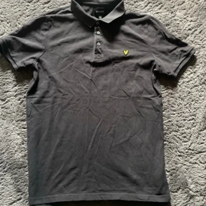 Svart pikétröja från Lyle & Scott - Svart pikétröja från Lyle & Scott. Knapparna sitter lite löst i kragen.