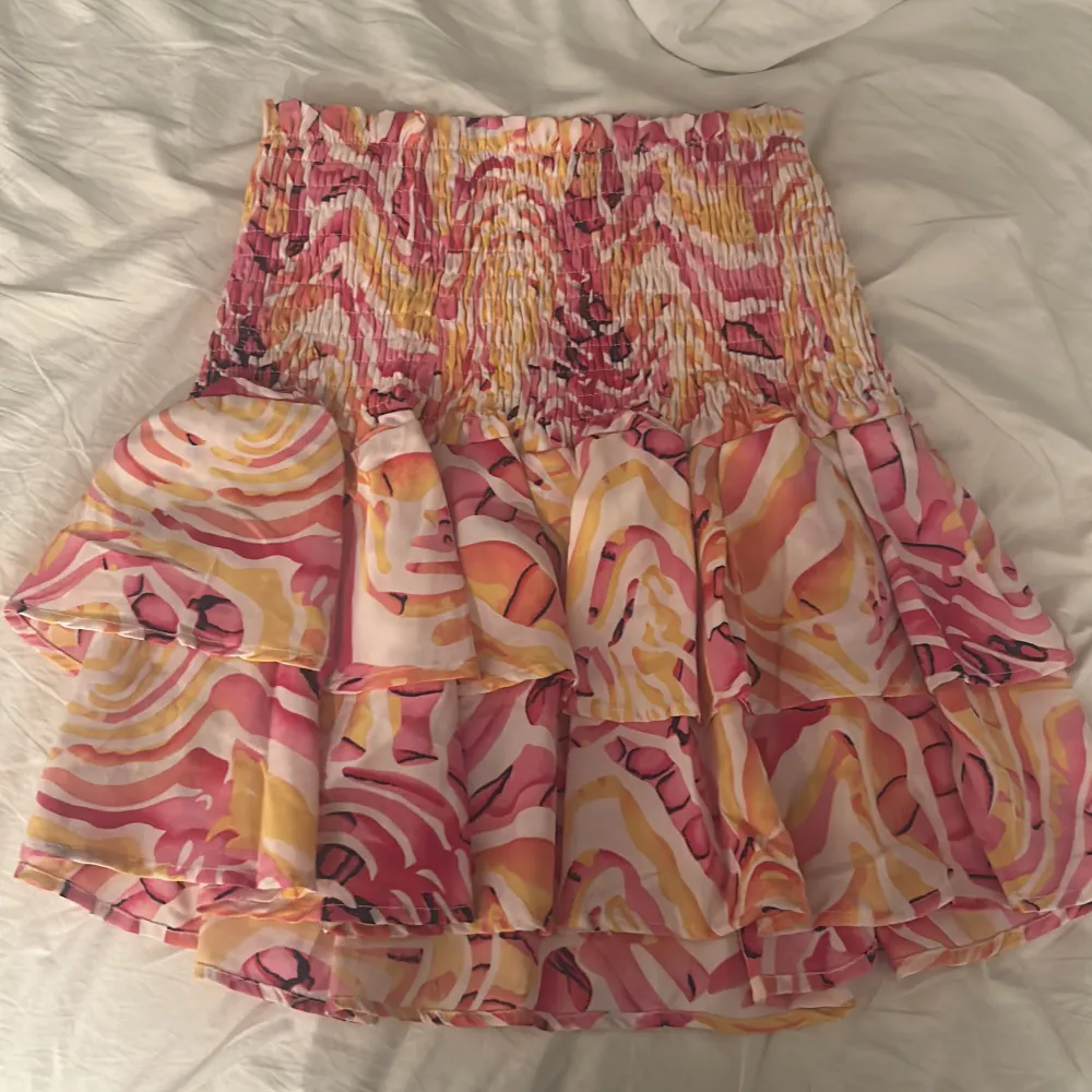 Säljer en färgglad kjol från Yu & Me med ett abstrakt mönster i rosa, gul och orange. Kjolen har en volangdetalj och en elastisk midja för en bekväm passform. Perfekt för att liva upp garderoben!. Hameet.