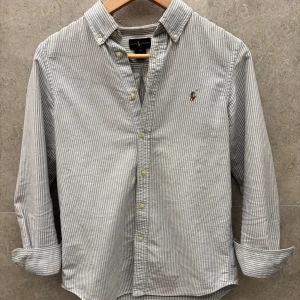 Randig skjorta från Ralph Lauren - Snygg randig skjorta från Ralph Lauren i blått och vitt. Skick 8/10 Skjorta är endast använd ett fåtal gånger | Storlek: 14/Xxs (passar optimalt runt 160cm) | Nypris ligger på 1399kr | Det är bara att skriva om ni har frågor eller funderingar!