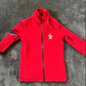 Röd Moncler kofta  - Snygg röd tröja från Moncler med dragkedja och hög krage. Riktigt skön, modellen heter Moncler Grenoble. Mer bilder finns vid behov 🍾✅🥂riktigt bra skick helt ny 