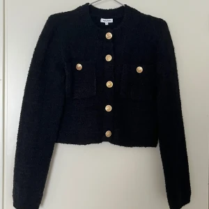 Svart kavaj  - Snygg svart kavaj med guldknappar och två framfickor. Perfekt för en stilren look. Kavajen har en klassisk design med långa ärmar och en rak passform.