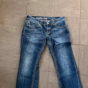 Blå jeans från Harlow - Snygga blåa lågmidjade jeans från Harlow med klassisk femficksdesign och dekorativa sömmar på bakfickorna och är flared. Jeansen har en knapp och dragkedja framtill samt en bekväm passform. Perfekta för en avslappnad stil.