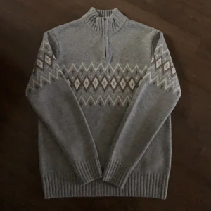 Bläck tröja - Säljer en extremt fin och välstickad grå tröja från det fina märket Bläck med ett klassiskt mönster i vitt och beige. Tröjan har en dragkedja vid halsen och långa ärmar. Perfekt för kyliga dagar. Endast använd 1-2 gånger så i stort sett som helt ny i skicket. Nypris 999kr, kan tänka mig gå i pris vid snabb affär👍🏻🙌🏻 