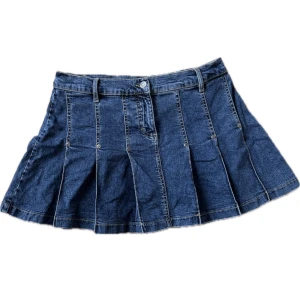 Blå jeanskjol - Snygg blå mini skirt jeanskjol med veckad design och knappdetaljer framtill. Kjolen har bälteshällor och en klassisk jeanslook som passar perfekt för en avslappnad stil. 