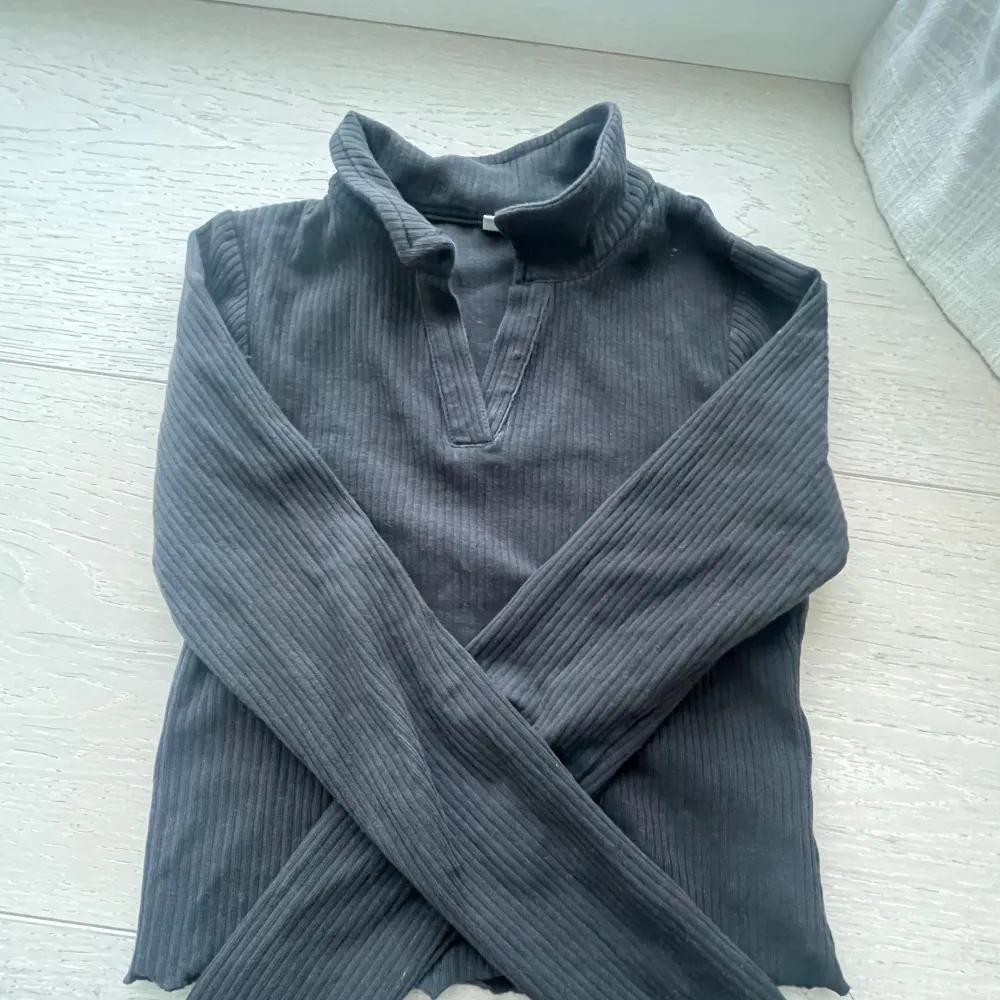 Säljer en stilren mörk grå ribbad tröja från Kappahl. Tröjan har långa ärmar och en unik krage med v-ringad detalj. Perfekt för en avslappnad och trendig look. Passar bra till både jeans och kjol. 🖤. Neuletakit & Villapaidat.