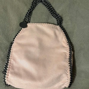 Rosa axelväska med kedjedetaljer - Snygg rosa axelväska med kedjedetaljer och leopardmönstrat foder. Väskan har en unik design med kedjor längs kanterna och en praktisk storlek för vardagsbruk. Perfekt för att ge din outfit en cool touch.