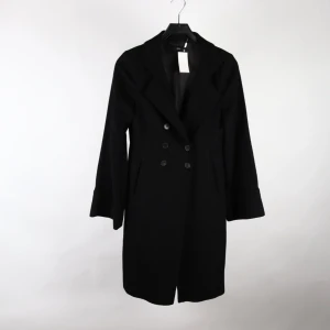 Elegant svart ullkappa från Hugo Boss – tidlös design i alpacka & ull - Lyxig och stilren kappa från Hugo Boss i en exklusiv ull- och alpackablandning. Klassisk figursydd modell med dubbelknäppning och elegant snitt som passar både till vardags och fest. Storlek 34 och i mycket gott skick.  Perfekt för dig som söker en sofistikerad och tidlös ytterrock av hög kvalitet.  📦 Skickas snabbt och säkert. Ingen prutning.