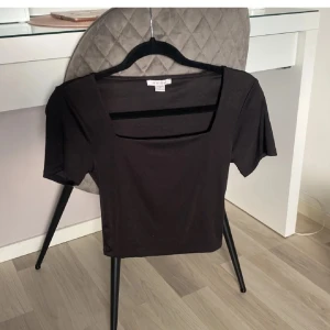 Svart kortärmad topp från Amisu - Snygg svart topp från Amisu med fyrkantig halsringning. Den har korta ärmar och en stilren design som passar perfekt till olika outfits. Perfekt för både vardag och speciella tillfällen.