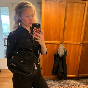 Svart axelväska med randigt foder - Säljer en snygg svart liten axelarm väska. Jag har inte använt väskan mycket och den är väl omhändertagen. Väskan är perfekt för skolan eftersom den har flera fickor och den är i en perfekt storlek. Priset kan diskuteras💕🥰