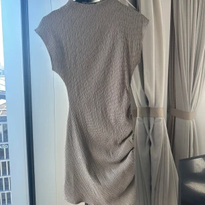 Beige klänning från Zara - Säljer en stilren beige klänning från Zara med en texturerad yta. Klänningen har en enkel design med korta ärmar och en rund halsringning. Perfekt för en minimalistisk look. Oanvänd!