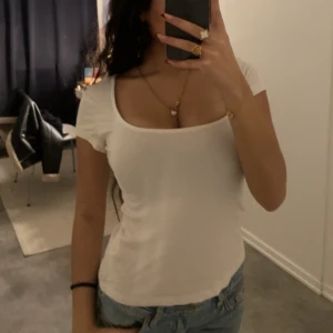 Vit ribbad topp från Kappahl - Säljer en stilren vit ribbad topp från Kappahl. Toppen har en fyrkantig ringning och korta ärmar, perfekt för en avslappnad look. Passar bra till jeans eller kjol. Hör av dig vid intresse!