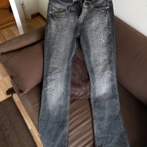 Gråa Jeans med glitter från Request - Jeans från Request i grått med snygga detaljer och pärlor. Älskar men använder aldrig. Storlek 30 men stretchigt material. Har ett hål vid midjebandet men inget som syns mycket! Hoppas att de hittar ett nytt fint hem! Midja 40 cm och ibl 81 cm