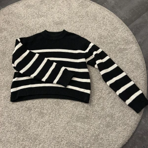 Svart och vit randig stickad tröja - Säljer en snygg svart och vit randig stickad tröja med långa ärmar. Perfekt för kyligare dagar och ger en stilren look. Tröjan har en klassisk passform och är supermjuk. Passar perfekt till jeans eller kjol!