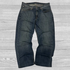 Levi's jeans  - Klassiska Levi's jeans i mörkblå denim med fem fickor och knappgylf. De har en rak passform och är perfekta för en avslappnad stil. Levi's ikoniska läderpatch finns på baksidan av midjan.