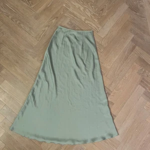 Grön långkjol från Amisu - Elegant grön långkjol från Amisu i ett mjukt och flödande material. Kjolen har en stilren design som passar perfekt för olika tillfällen. Den är i en vacker grön nyans och har en smickrande passform.