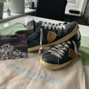 Philippe Model sneakers i blått skinn - Säljer ett par Philippe Model sneakers i blått skinn med grå mockadetaljer och vit sula. Skorna har vit snörning och en ikonisk sköldlogga på sidan. Dom är slitna i sula, men inga hål.
